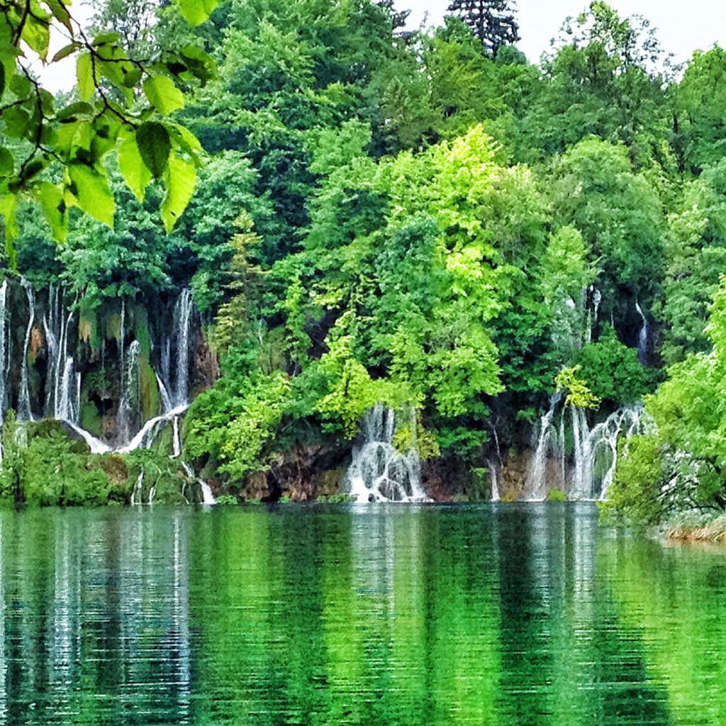 Beautiful waterfalls streaming into a green lake, surrounded by lush brush