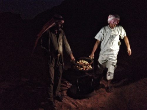 2 Bedouins carrying dinner from the sand to the tent