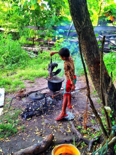 A small child cooking the losing rooster from a local cock fight in the Philippines. 