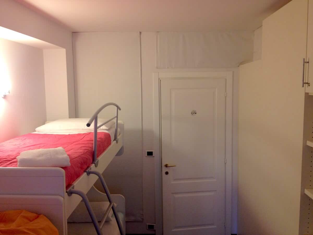 Small hostel room with bunk bed, white walls, and minimal decor.