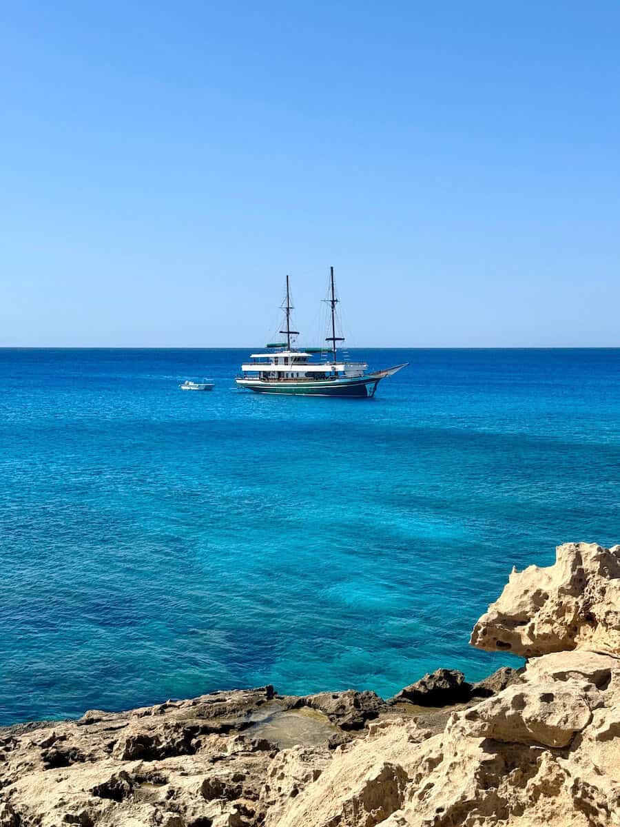 Luxury yacht sailing in clear blue Cyprus sea with rocky shoreline.