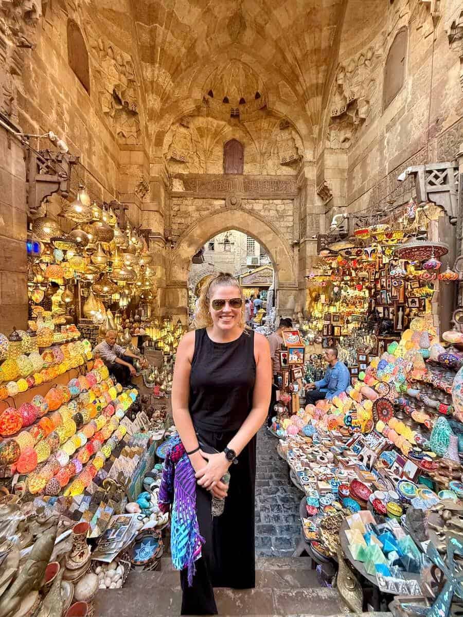 Woman shopping at a colorful market stall in Egypt with traditional architecture.