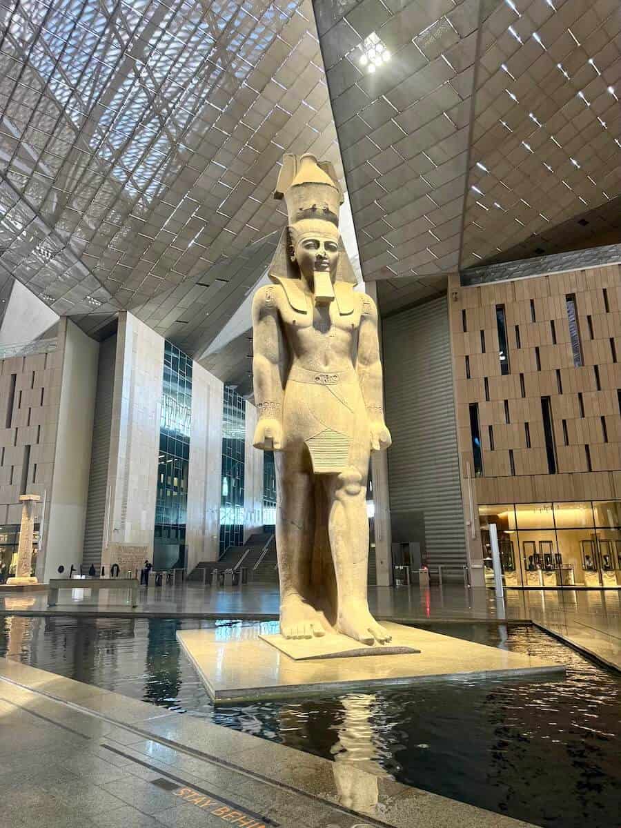 Large ancient Egyptian statue with a headdress in a modern museum setting.