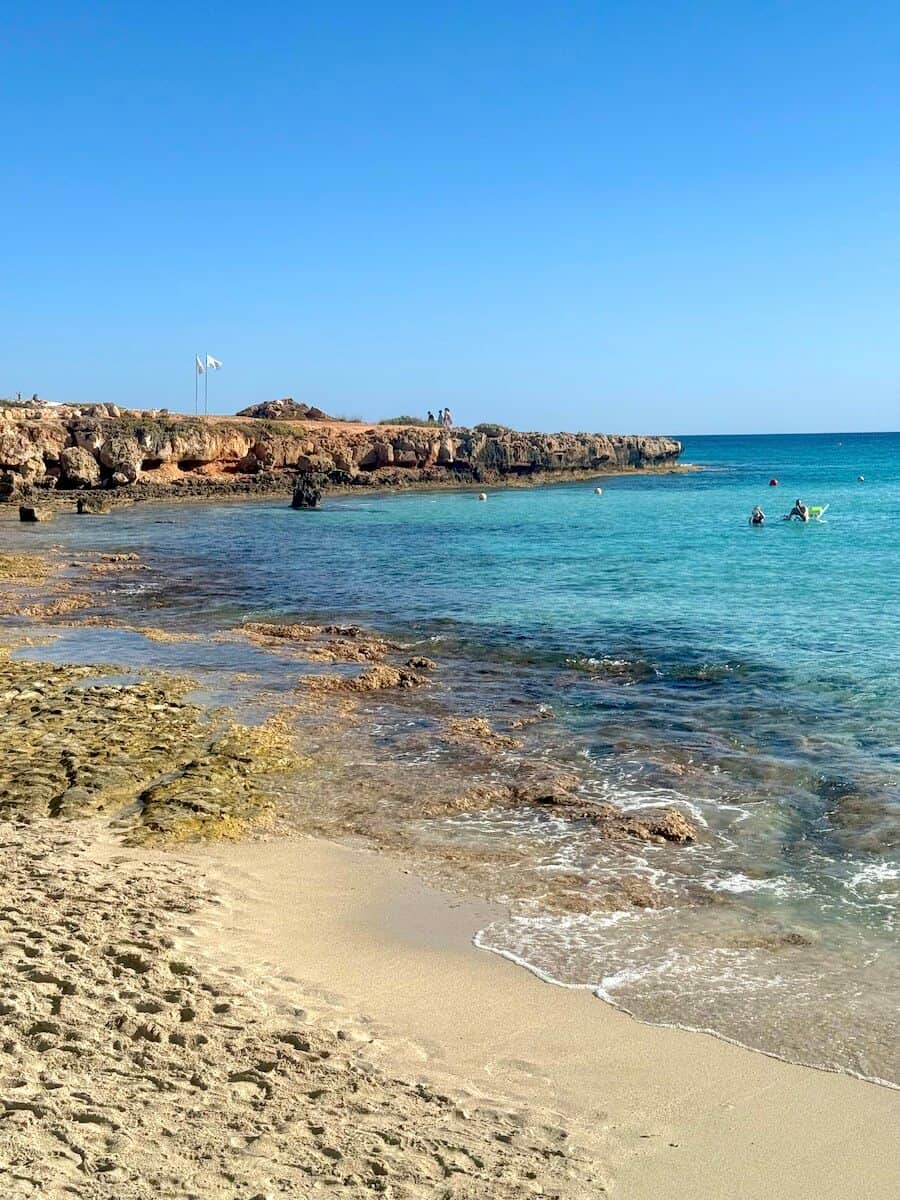 Beautiful Cyprus beach with clear blue water and rocky shoreline.