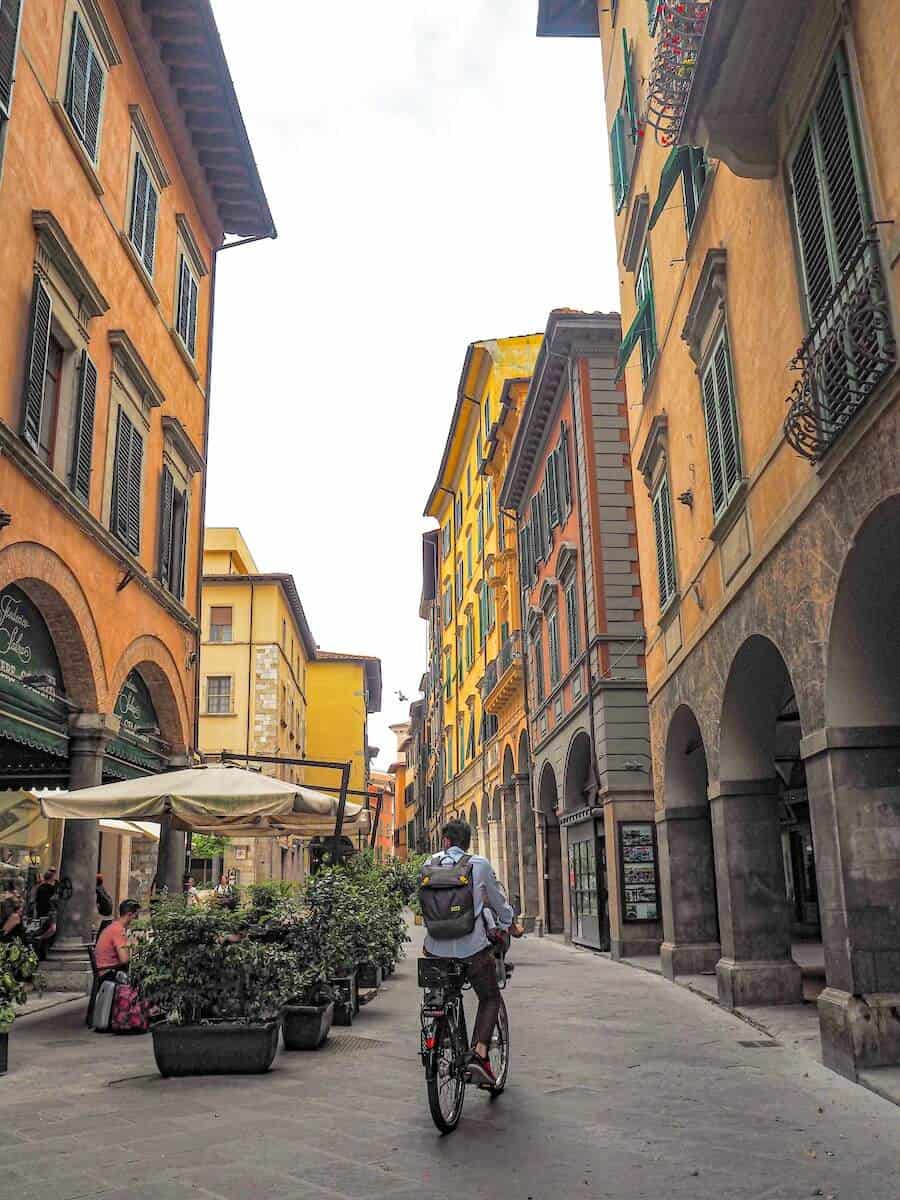 Cyclist riding through colorful historic street in Pisa, Italy.