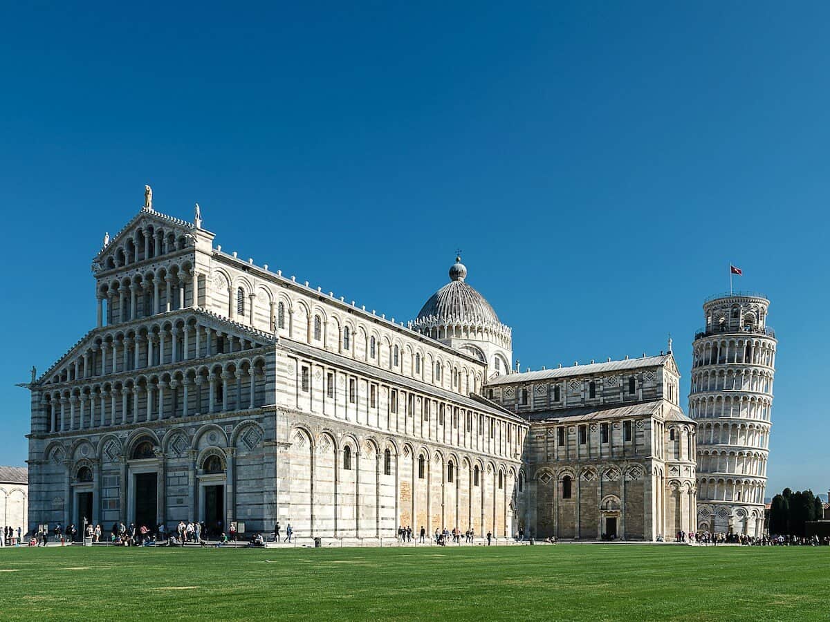 Iconic Leaning Tower of Pisa with Cathedral in Pisa, Italy under clear blue sky.
