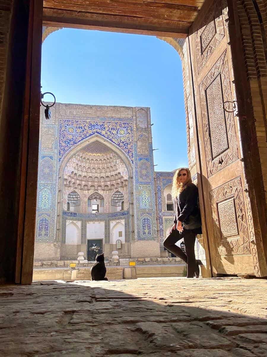 Woman standing at a historic Islamic building with intricate tile work and a cat nearby.